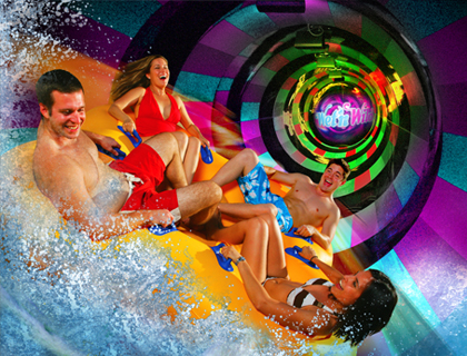 A group of people, two women and two men, use a four-person water tube to slide through an enclosed slide at Wet & Wild Water Park.