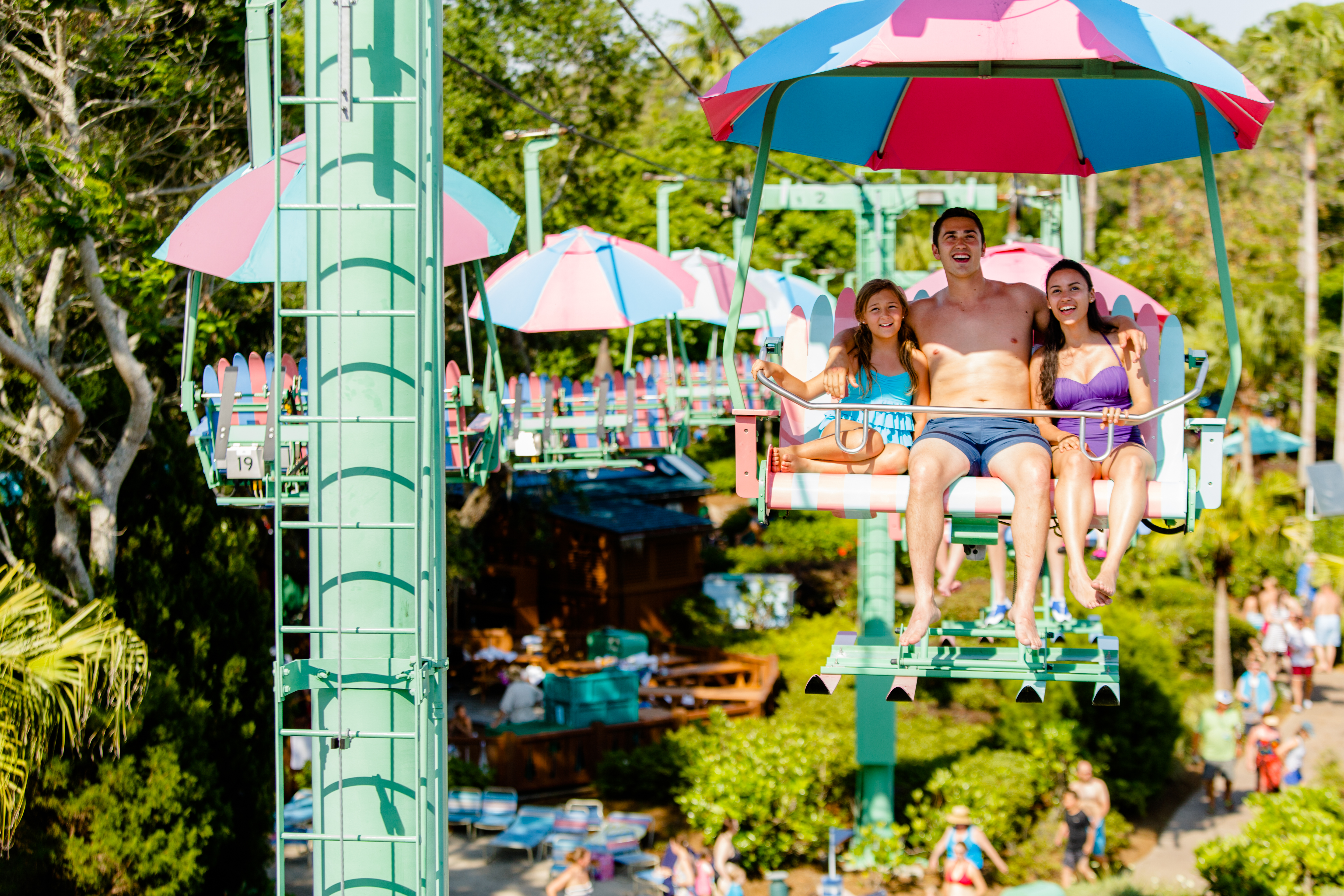 A guy, a little girl and an adult woman ride on a ski lift at Disney's Blizzard Beach during the daytime.