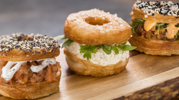 Three styles of bagel-shaped sandwiches (Trio of Savory Croissant Doughnuts) on wooden slab for Epcot International Festival of the Arts.