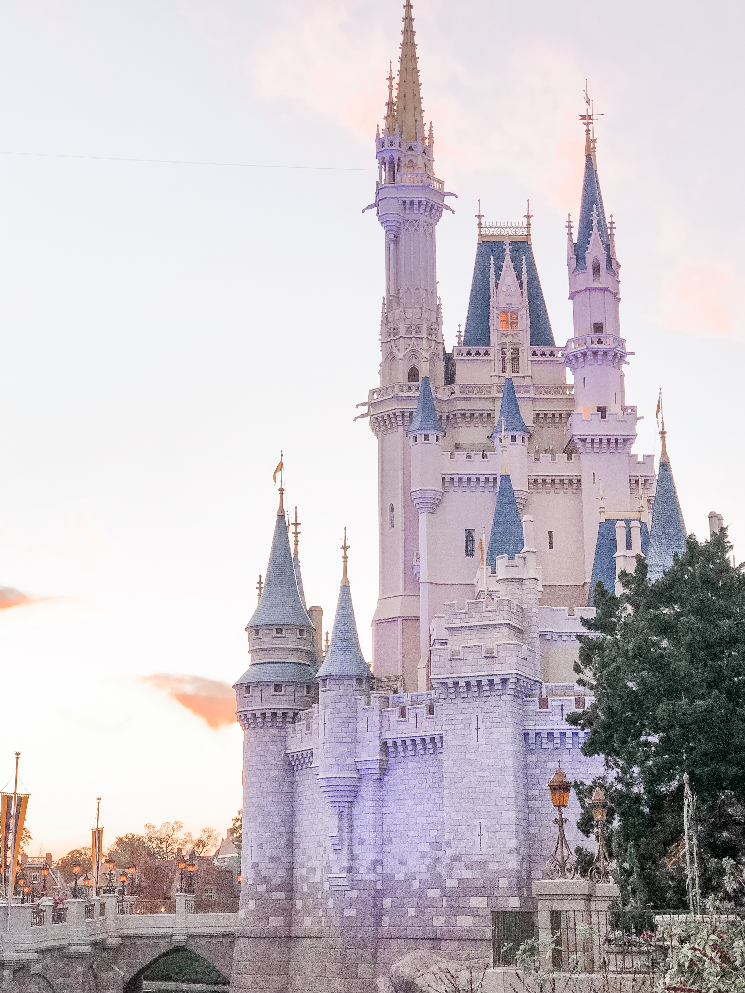 A side view of Cinderella's Castle at Disney's Magic Kingdom (right side) with hues of purple and pink lighting throughout the outside of the castle during beginning sunset stages.