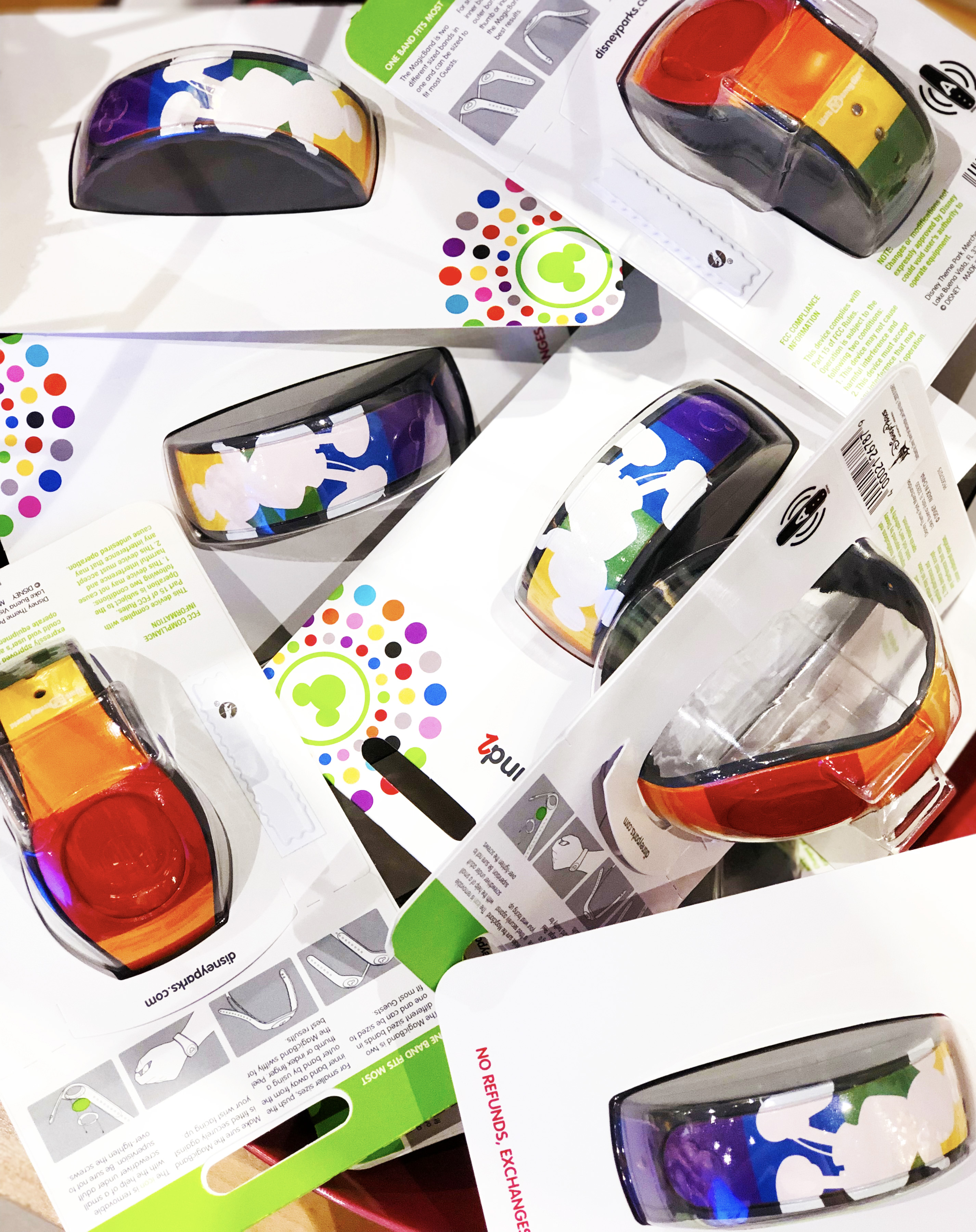 A pile of packaged MagicBands designed with a white silhouette of Mickey Mouse and a striped-rainbow band.