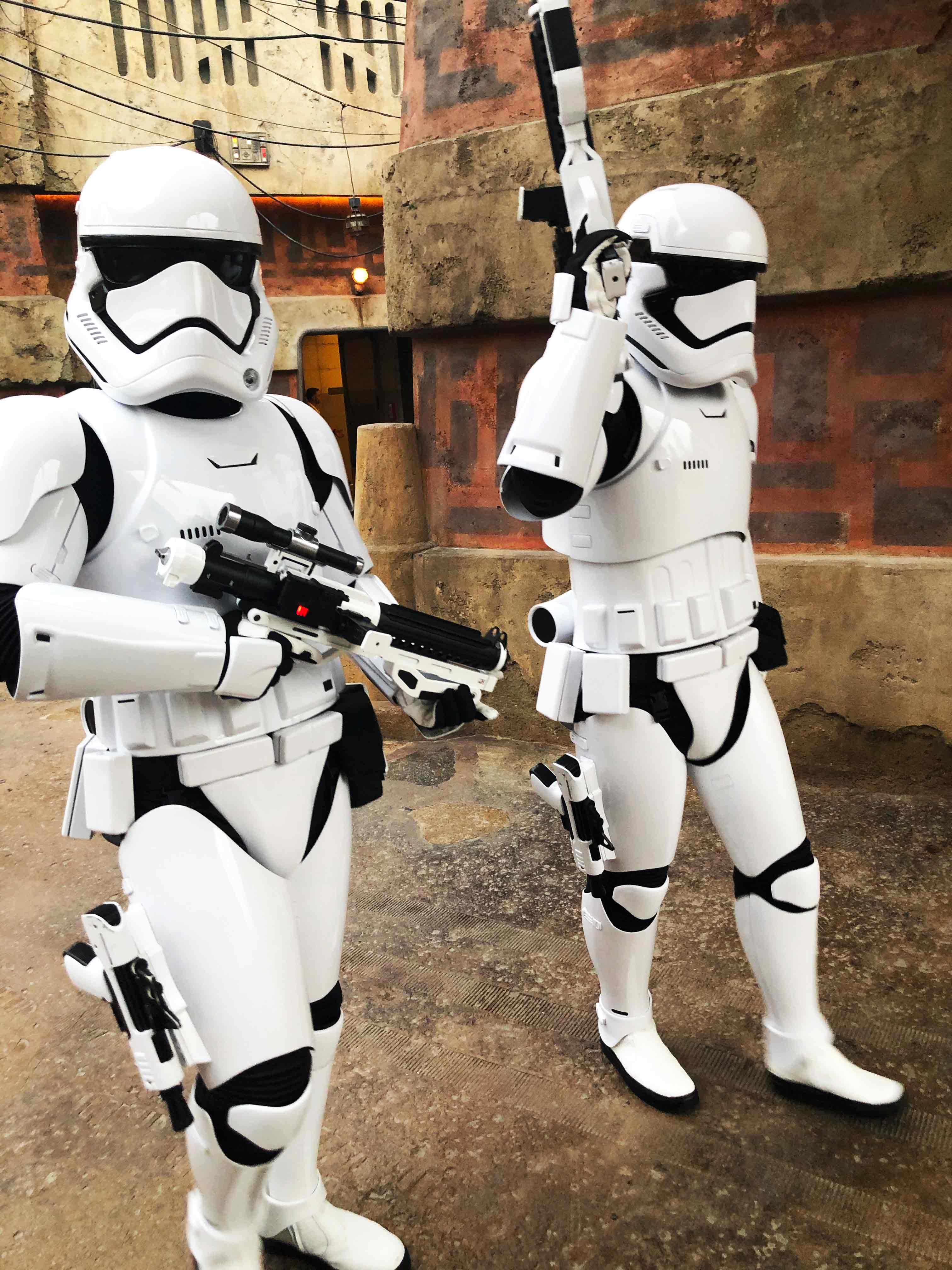 Daytime shot of two Storm Troopers, one holding trooper gun with both hands (left) and other pointing trooper gun up (right) as both walk through Batuu inside of Star Wars: Galaxy's Edge at Disney's Hollywood Studios®.