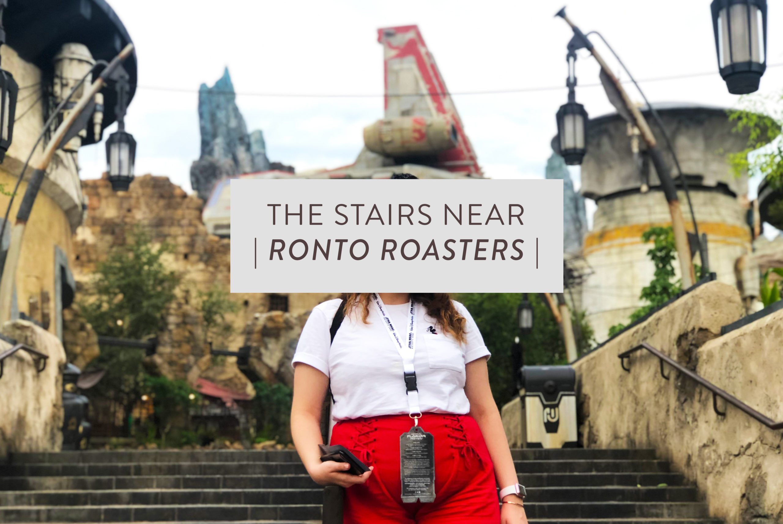 Woman posing (face covered by boxed text) on stairs near Ronto Roasters with Batuu in the background, daytime shot, inside of Star Wars: Galaxy's Edge at Disney's Hollywood Studios®. Lake Buena Vista, Florida.