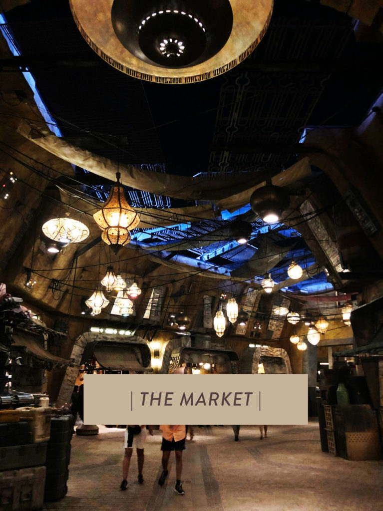 An evening shot of a lit up Market inside of Star Wars: Galaxy's Edge at Disney's Hollywood Studios®. Boxed text with "The Market" typed in it on the lower center of the photo. Lake Buena Vista, Florida.
