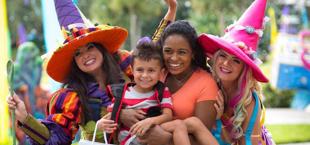 Two women (left and right) dressed as friendly witches smiling for the camera with a son being held by his mom mom (center) for SeaWorld Orlando's Halloween Spooktacular®, Orlando, Florida.