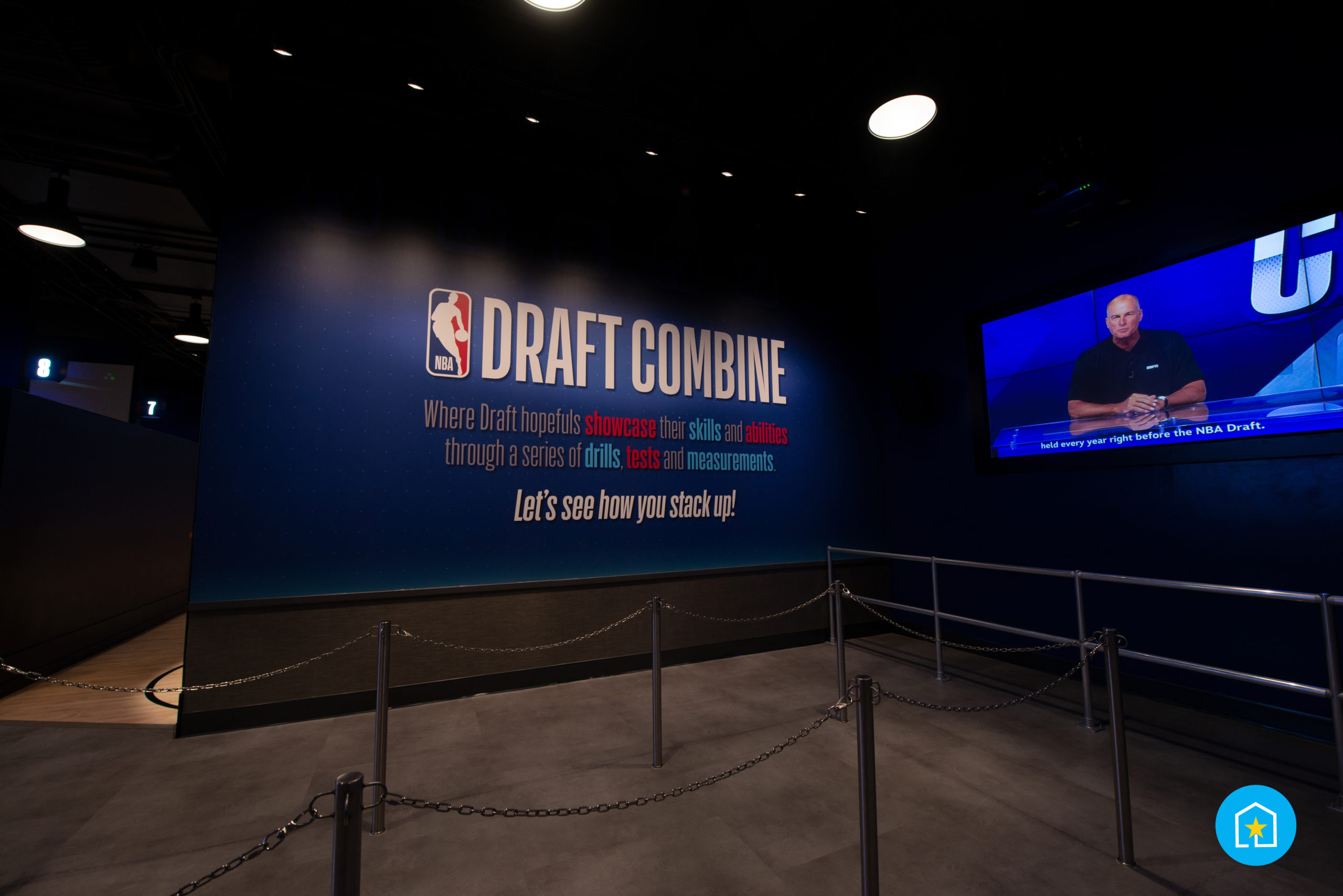 Photo of Draft Combine wall and TV screen (on right) in the queue for Draft Combine. Wall reads "Draft Combine, Where Draft hopefuls showcase their skills and abilities through a series of drills, tests and measurements, Let's see how you stack up!", TV features man sitting at desk on recorded broadcast. The NBA Experience, Disney Springs, Lake Buena Vista, Florida.