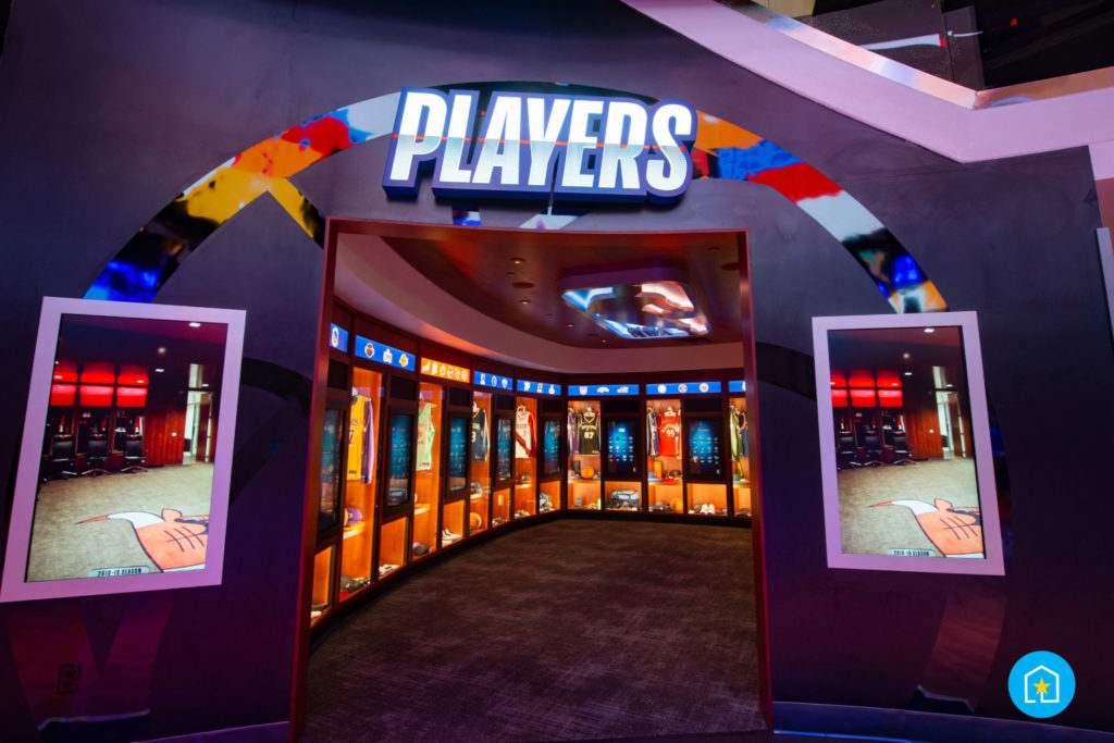 Entrance of Players inside of the NBA Experience at Disney Springs® (Lake Buena Vista, Florida). Entrance shows "PLAYERS" at top of photo with rectangular-shaped room that has multiple large touch screens and basketball memorabilia.