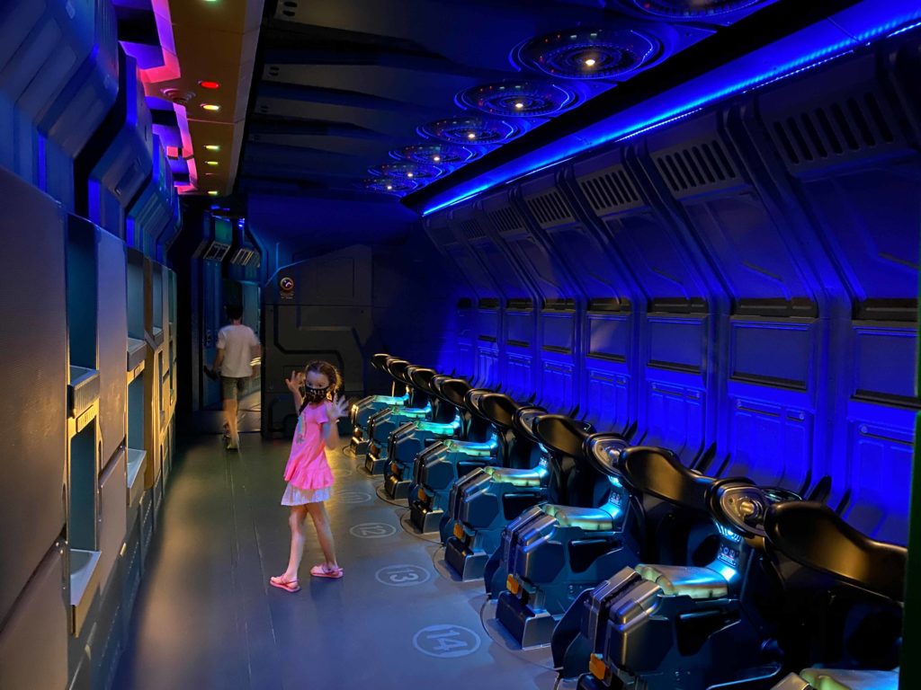 Indoor photo of boy walking down the attraction corridor (top left corner) and girl (center) turned around posing for the camera as she stands beside the bikes in Avatar: Flight of Passage at Disney's Animal Kingdom® Theme Park. Lake Buena Vista, Florida.