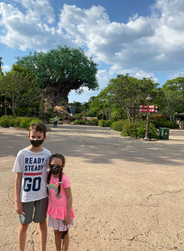 Daytime shot of boy and girl (left corner) posing for photo with the Tree of Life in the distance and a very empty Disney's Animal Kingdom® Theme Park in the background. Lake Buena Vista, Florida.