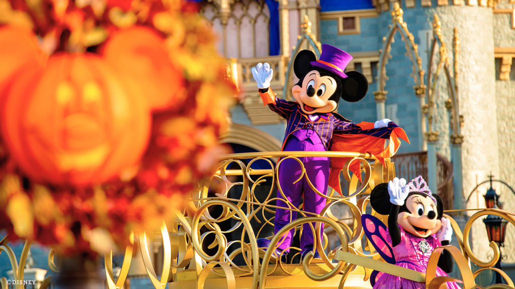 Daytime photo of Mickey (center) and Minnie Mouse (lower right) dressed in purple Halloween attire on a float at the Magic Kingdom® Park. Blurred Mickey Pumpkin hands on a light pole on the left of the photo. 2020. Lake Buena Vista, Florida.