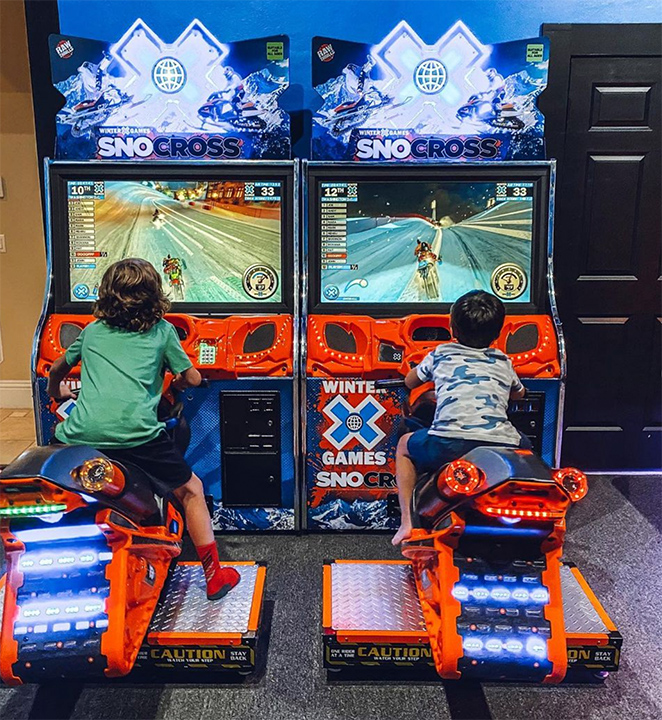 Two kids playing on the SnoCross arcade game at RVH_441M. Magical Stays. Instagram, @nippersnook.