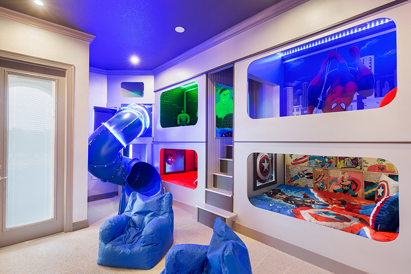 Superhero-inspired bedroom featuring two built-in bunk beds and a blue slide with LED strip lighting. Designed for Vacation (RVH_320M) in Reunion Resort. Kissimmee, Florida.
